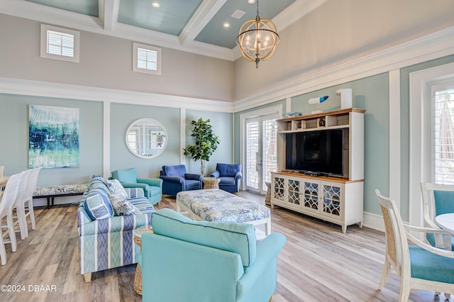 living room with a towering ceiling, ornamental molding, wood-type flooring, beam ceiling, and an inviting chandelier