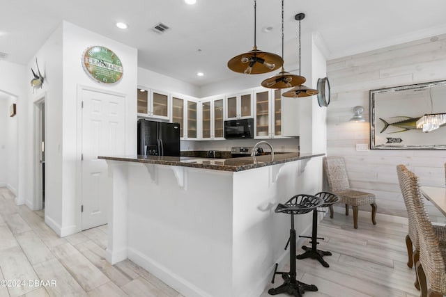 kitchen featuring a breakfast bar, black appliances, wooden walls, decorative light fixtures, and kitchen peninsula