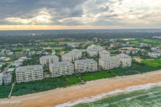 aerial view at dusk featuring a view of the beach and a water view