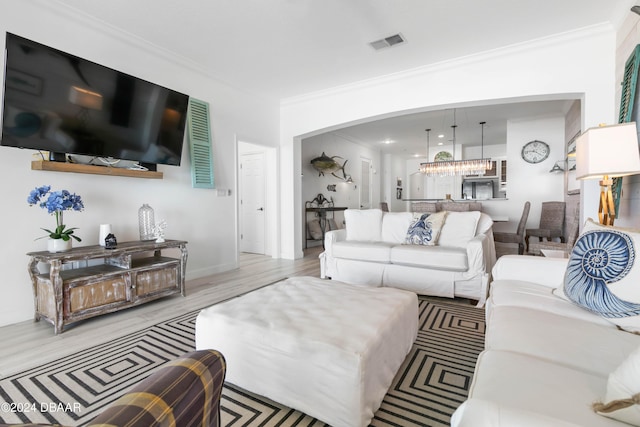 living room featuring a chandelier, light wood-type flooring, and ornamental molding