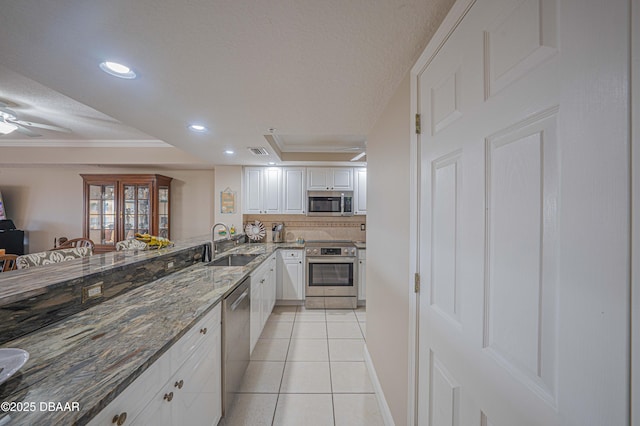 kitchen with appliances with stainless steel finishes, white cabinetry, sink, dark stone counters, and a tray ceiling