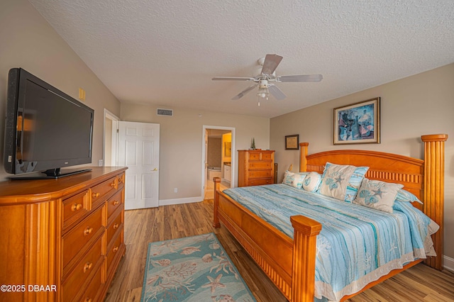 bedroom with ceiling fan, connected bathroom, a textured ceiling, and hardwood / wood-style floors