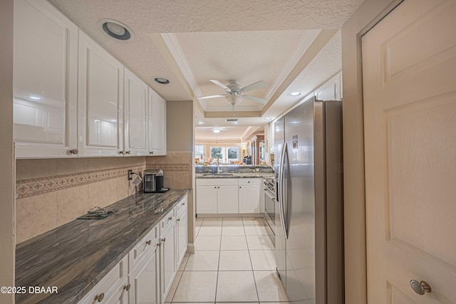 kitchen with a raised ceiling, appliances with stainless steel finishes, white cabinetry, light tile patterned floors, and a textured ceiling