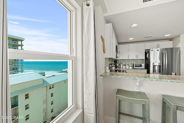 3721 S Atlantic Ave Unit 801, Daytona Beach Shores, FL 32116 - kitchen with stainless steel fridge with ice dispenser, backsplash, white cabinets, light stone countertops, and range