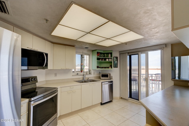 kitchen featuring appliances with stainless steel finishes, sink, light tile patterned flooring, and a textured ceiling