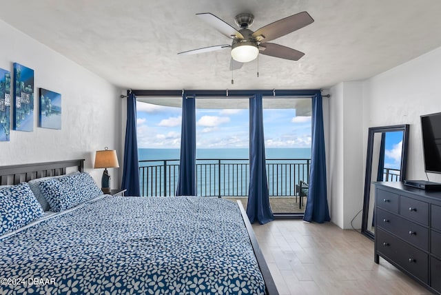 bedroom featuring light hardwood / wood-style floors, ceiling fan, multiple windows, and a water view