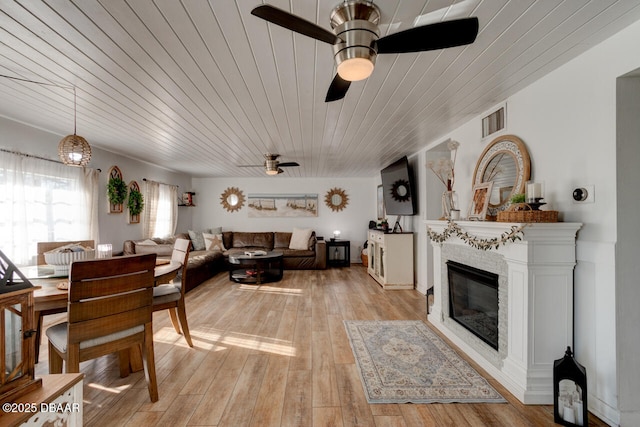 dining area featuring visible vents, light wood-style flooring, a ceiling fan, a glass covered fireplace, and wood ceiling