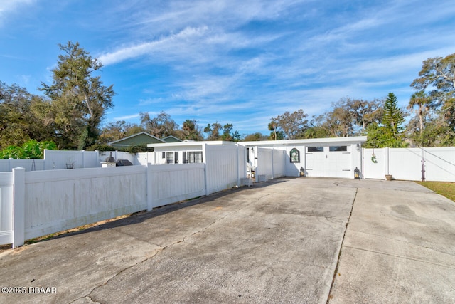 exterior space featuring a garage, concrete driveway, a fenced front yard, and a gate