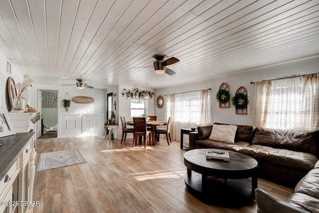 living area featuring a ceiling fan, wood ceiling, wainscoting, and light wood-style flooring