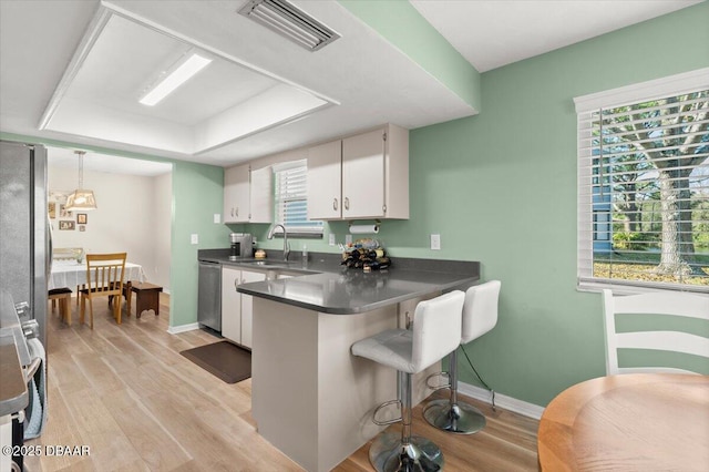 kitchen featuring appliances with stainless steel finishes, white cabinetry, sink, hanging light fixtures, and light hardwood / wood-style floors