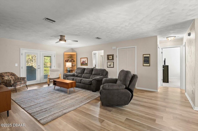 living room with french doors, a textured ceiling, and light wood-type flooring