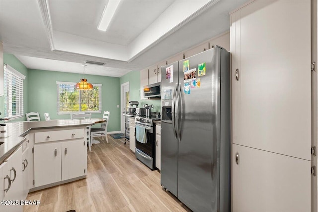 kitchen with appliances with stainless steel finishes, white cabinets, hanging light fixtures, light hardwood / wood-style floors, and a raised ceiling