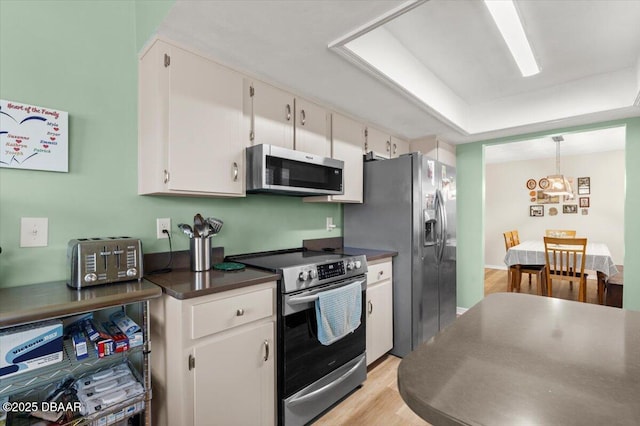 kitchen featuring pendant lighting, white cabinets, a tray ceiling, stainless steel appliances, and light wood-type flooring