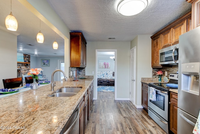 kitchen featuring appliances with stainless steel finishes, a textured ceiling, pendant lighting, sink, and light hardwood / wood-style flooring