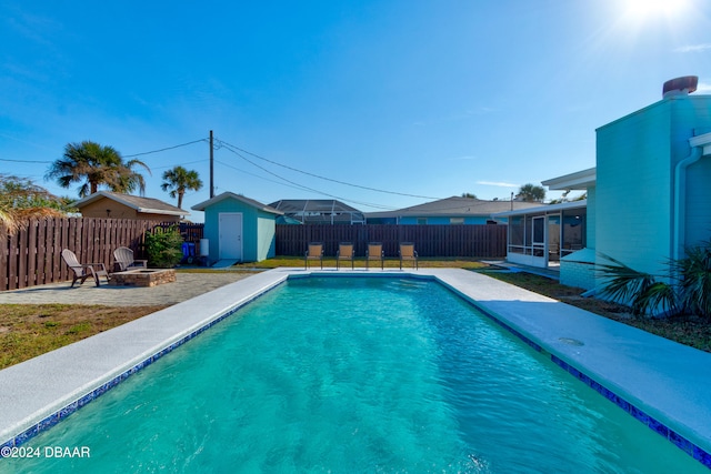 view of swimming pool featuring a sunroom, a fire pit, and a storage unit