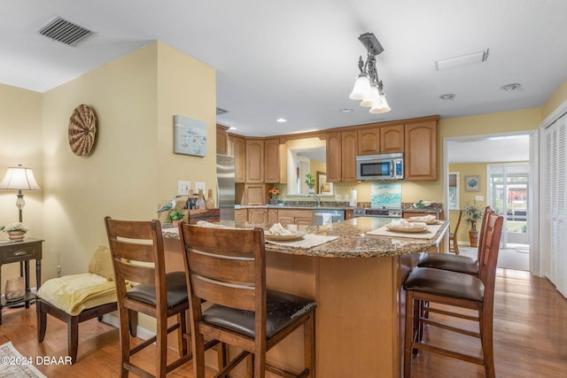 kitchen with kitchen peninsula, appliances with stainless steel finishes, wood-type flooring, decorative light fixtures, and dark stone countertops