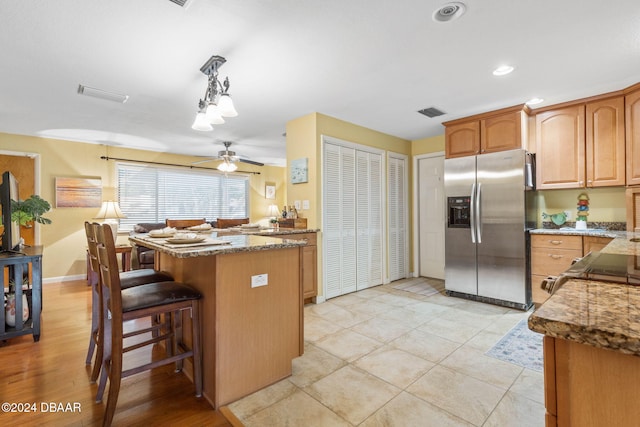 kitchen featuring ceiling fan, stainless steel fridge with ice dispenser, kitchen peninsula, decorative light fixtures, and a breakfast bar