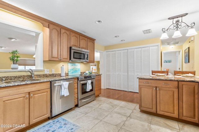 kitchen featuring sink, light stone counters, pendant lighting, light tile patterned floors, and appliances with stainless steel finishes