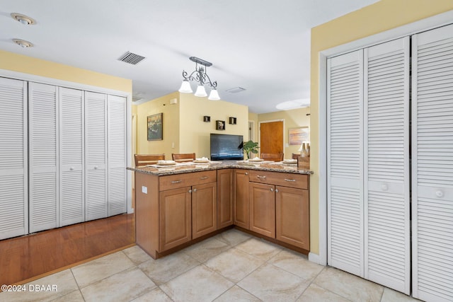 kitchen featuring decorative light fixtures, stone counters, kitchen peninsula, and light tile patterned floors