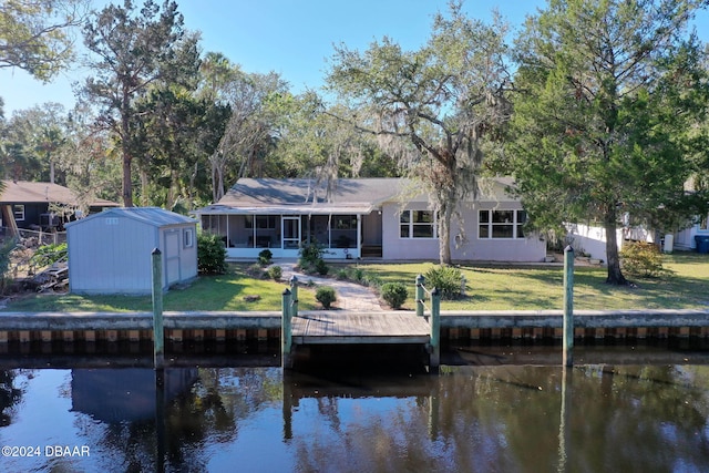 back of property with a sunroom, a yard, a water view, and a storage unit