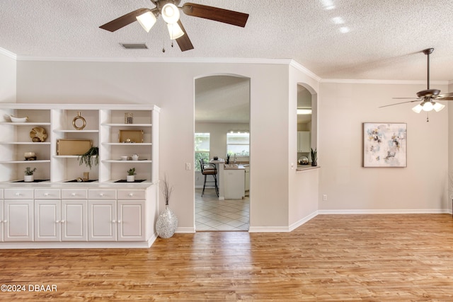 interior space featuring a textured ceiling, light wood-type flooring, ceiling fan, and crown molding