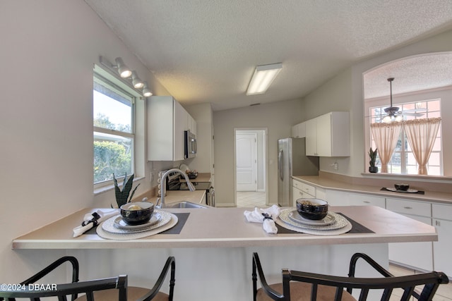 kitchen with pendant lighting, a breakfast bar, sink, appliances with stainless steel finishes, and white cabinetry