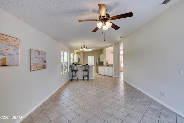 unfurnished living room featuring light tile patterned floors, ceiling fan with notable chandelier, and a textured ceiling