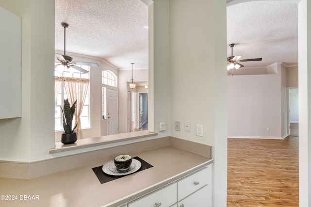 kitchen with white cabinets, light wood-type flooring, ornamental molding, and a textured ceiling