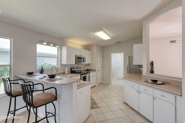 kitchen with kitchen peninsula, a healthy amount of sunlight, white cabinets, and stainless steel appliances