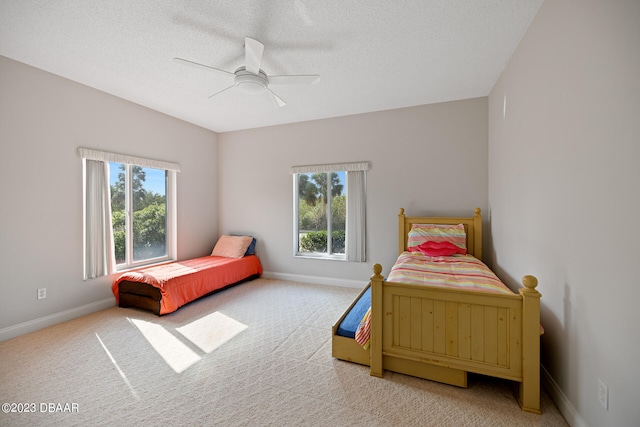 carpeted bedroom with ceiling fan, multiple windows, and a textured ceiling