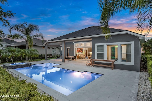 6294 W Fallsgrove Ln, Port Orange, FL 32128 - back of property at dusk with stucco siding, a patio area, a pool with connected hot tub, a ceiling fan, and roof with shingles