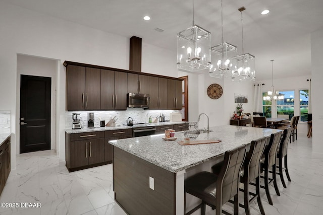 6294 W Fallsgrove Ln, Port Orange, FL 32128 - kitchen with stainless steel appliances, a chandelier, light marble finish flooring, a breakfast bar, and a towering ceiling