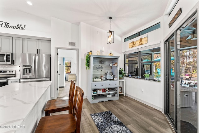 dining area featuring visible vents, vaulted ceiling, baseboards, and wood finished floors