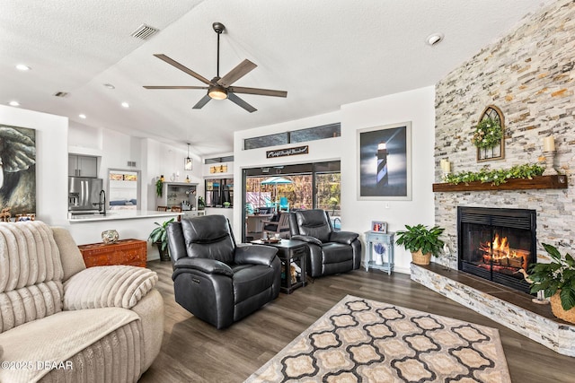 living room featuring visible vents, ceiling fan, wood finished floors, a textured ceiling, and a stone fireplace