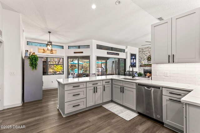 kitchen featuring dishwasher, a peninsula, gray cabinets, light countertops, and a sink