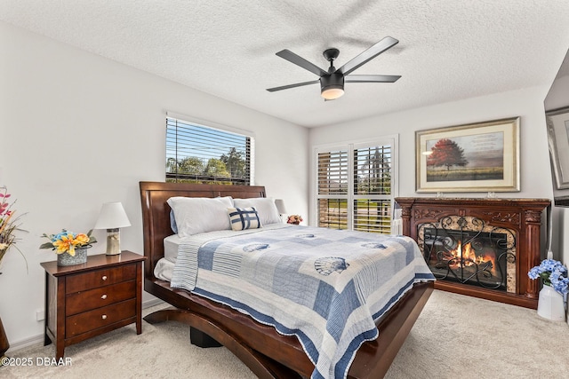 bedroom featuring a warm lit fireplace, a ceiling fan, a textured ceiling, and light colored carpet