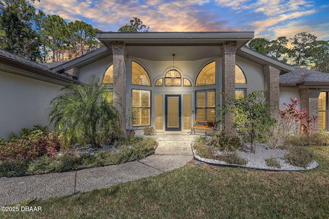 entrance to property with brick siding, a lawn, and stucco siding