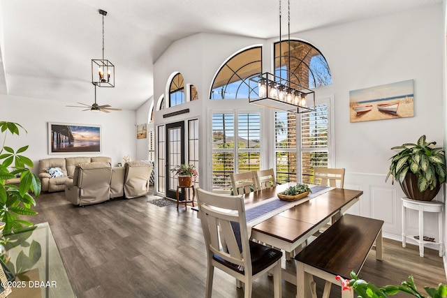 dining room with dark wood-style floors, wainscoting, high vaulted ceiling, and ceiling fan with notable chandelier