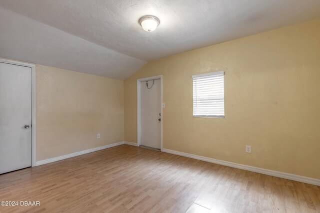 empty room featuring a textured ceiling, light hardwood / wood-style flooring, and lofted ceiling