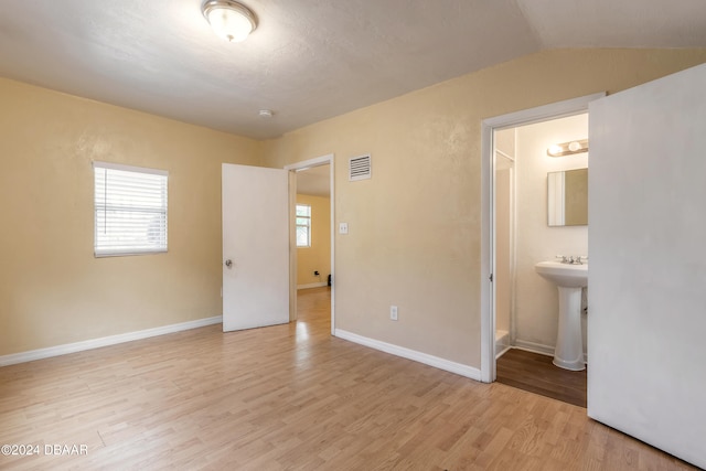 unfurnished bedroom with light hardwood / wood-style flooring, sink, vaulted ceiling, and ensuite bath