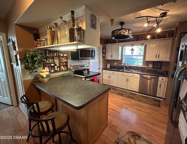 kitchen with appliances with stainless steel finishes, white cabinetry, sink, kitchen peninsula, and light wood-type flooring