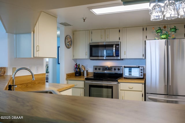 kitchen with appliances with stainless steel finishes, sink, pendant lighting, and butcher block countertops