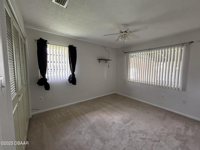 empty room featuring a textured ceiling, plenty of natural light, light colored carpet, and ceiling fan