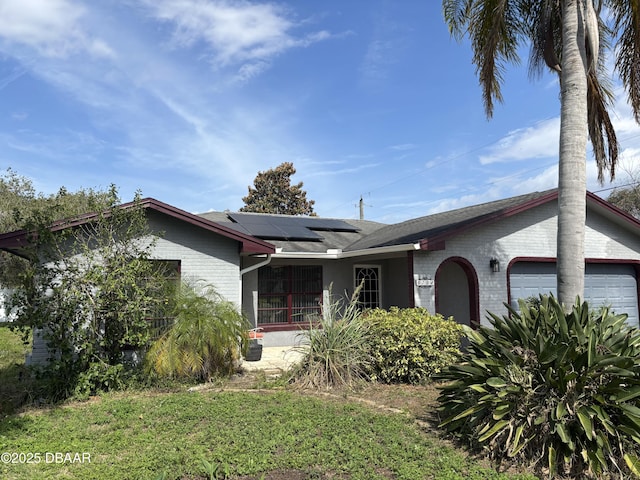 ranch-style home featuring a garage, a front lawn, and solar panels