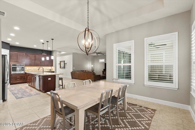 tiled dining space with ceiling fan with notable chandelier, a tray ceiling, and sink