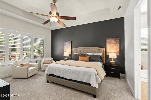 carpeted bedroom with a tray ceiling, connected bathroom, and ceiling fan