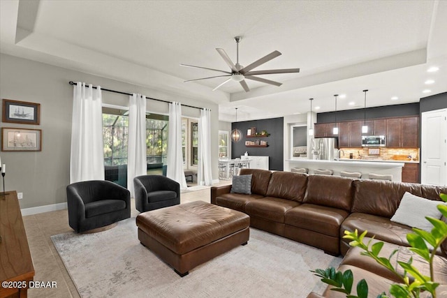 living room featuring ceiling fan, light tile patterned floors, and a tray ceiling