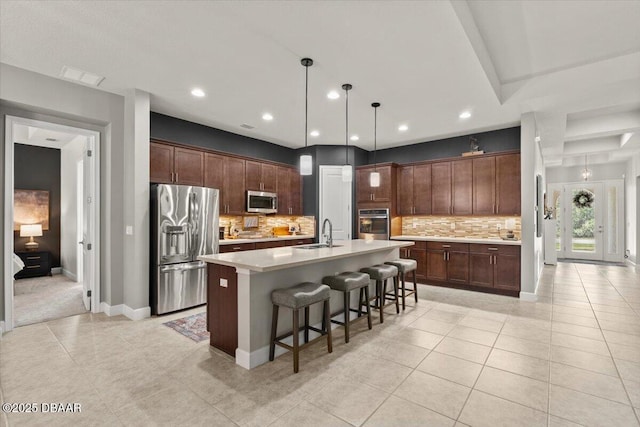 kitchen featuring backsplash, a kitchen island with sink, stainless steel appliances, and decorative light fixtures