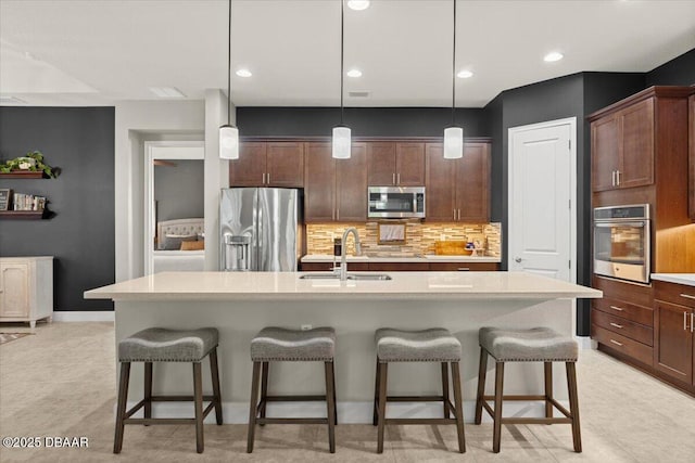 kitchen featuring pendant lighting, backsplash, a kitchen island with sink, sink, and stainless steel appliances