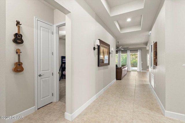 corridor featuring a tray ceiling and light tile patterned flooring